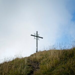 A cross stands on a grassy mountain summit.